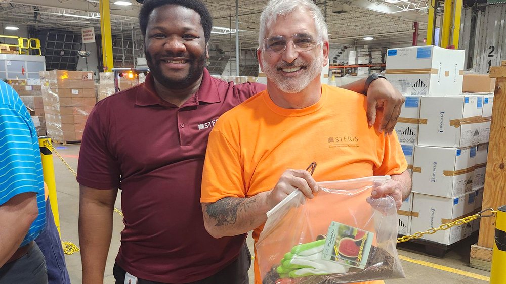 Two smiling STERIS colleagues standing arm in arm in a warehouse aisle