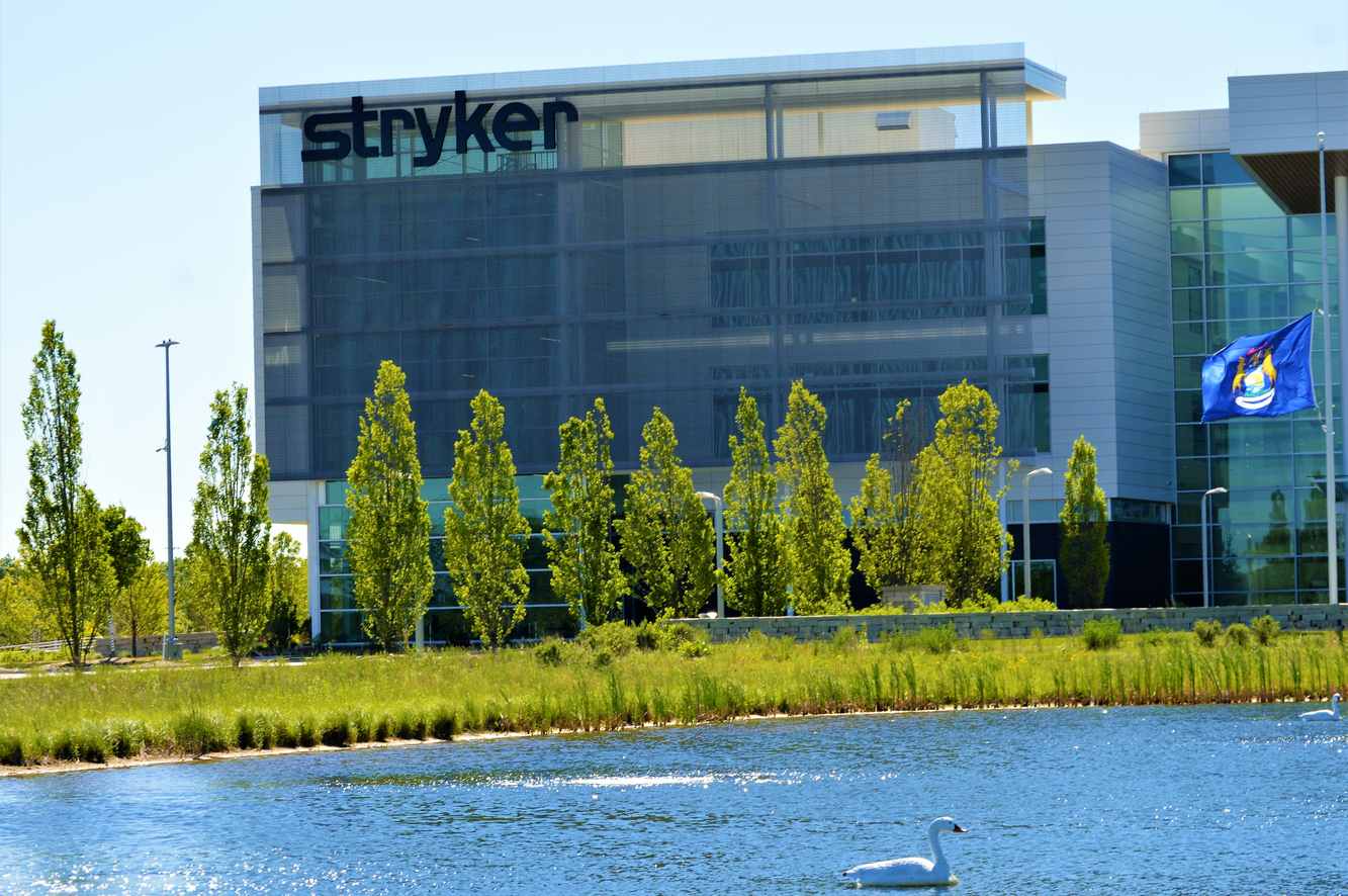 A Stryker office building in Michigan with the Stryker name on top, trees in front and a swan on a pond