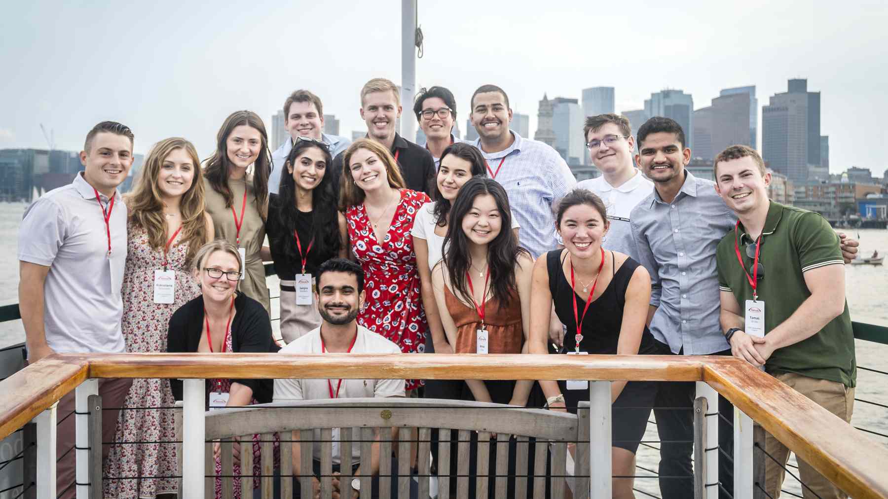 About twenty smiling Takeda interns with name badges posed on a deck with the Boston skyline behind