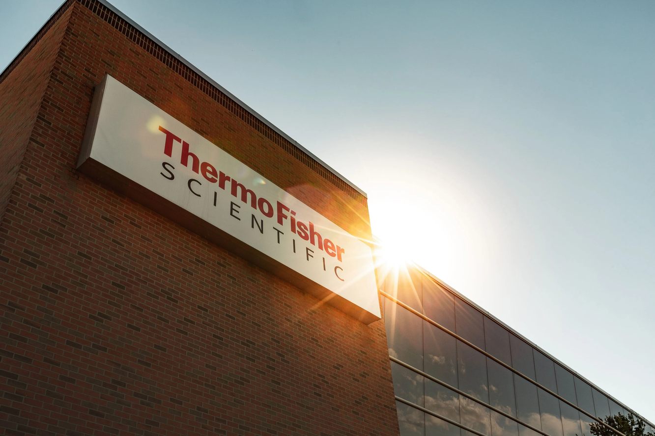 The Thermo Fisher Scientific name on a brick and glass building with the sun rising behind it