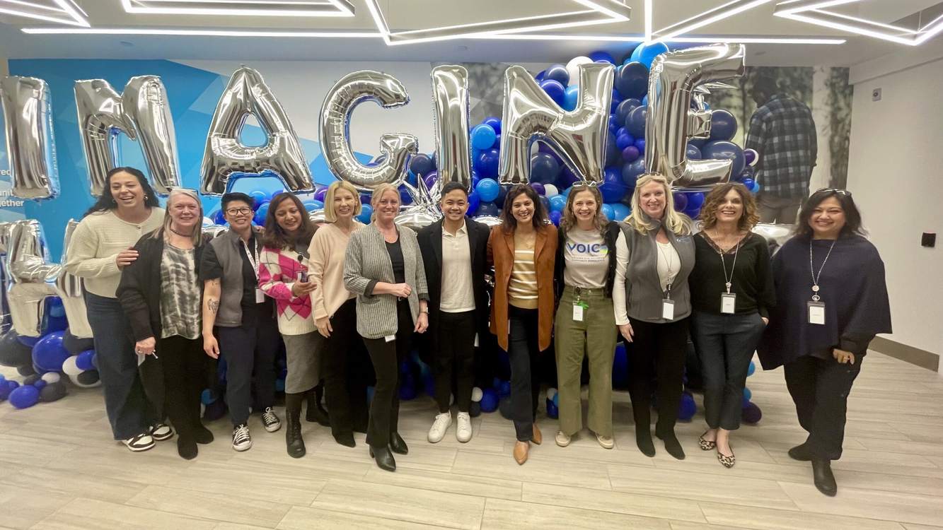Smiling Travere colleagues standing together under silver IMAGINE balloon letters in their office