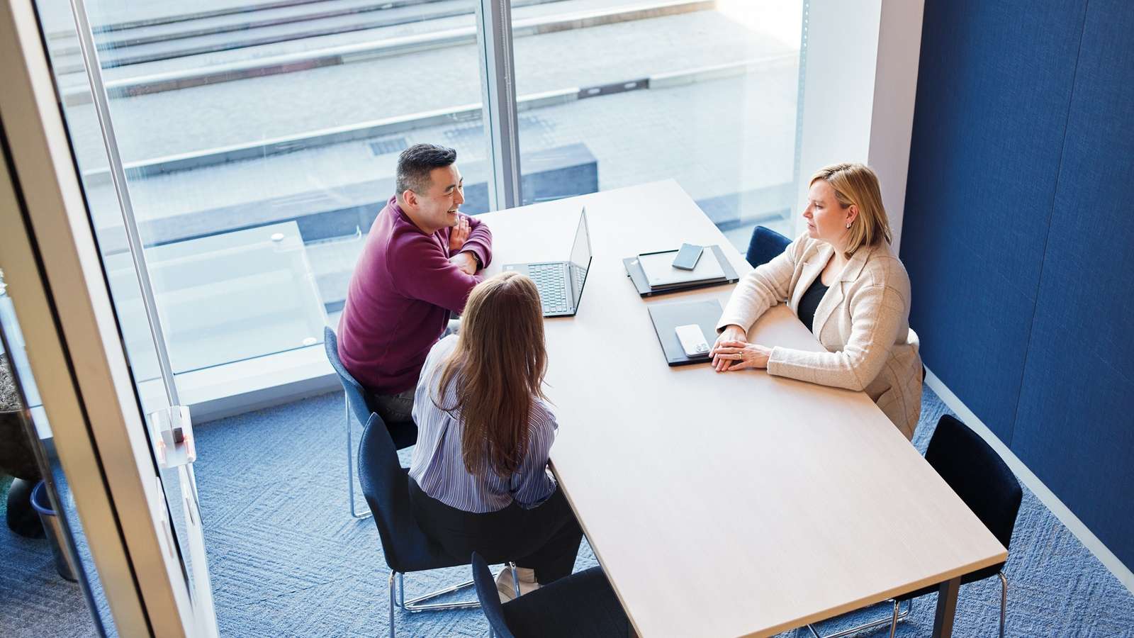 Three Vaxcyte colleagues talking around a table in a sunlit meeting room, seen from above
