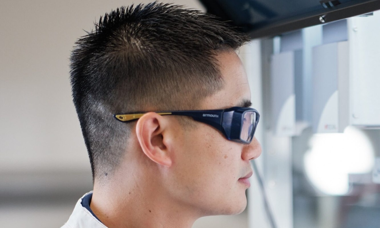 A Vaxcyte scientist in safety glasses and a branded lab coat working at an automated lab system