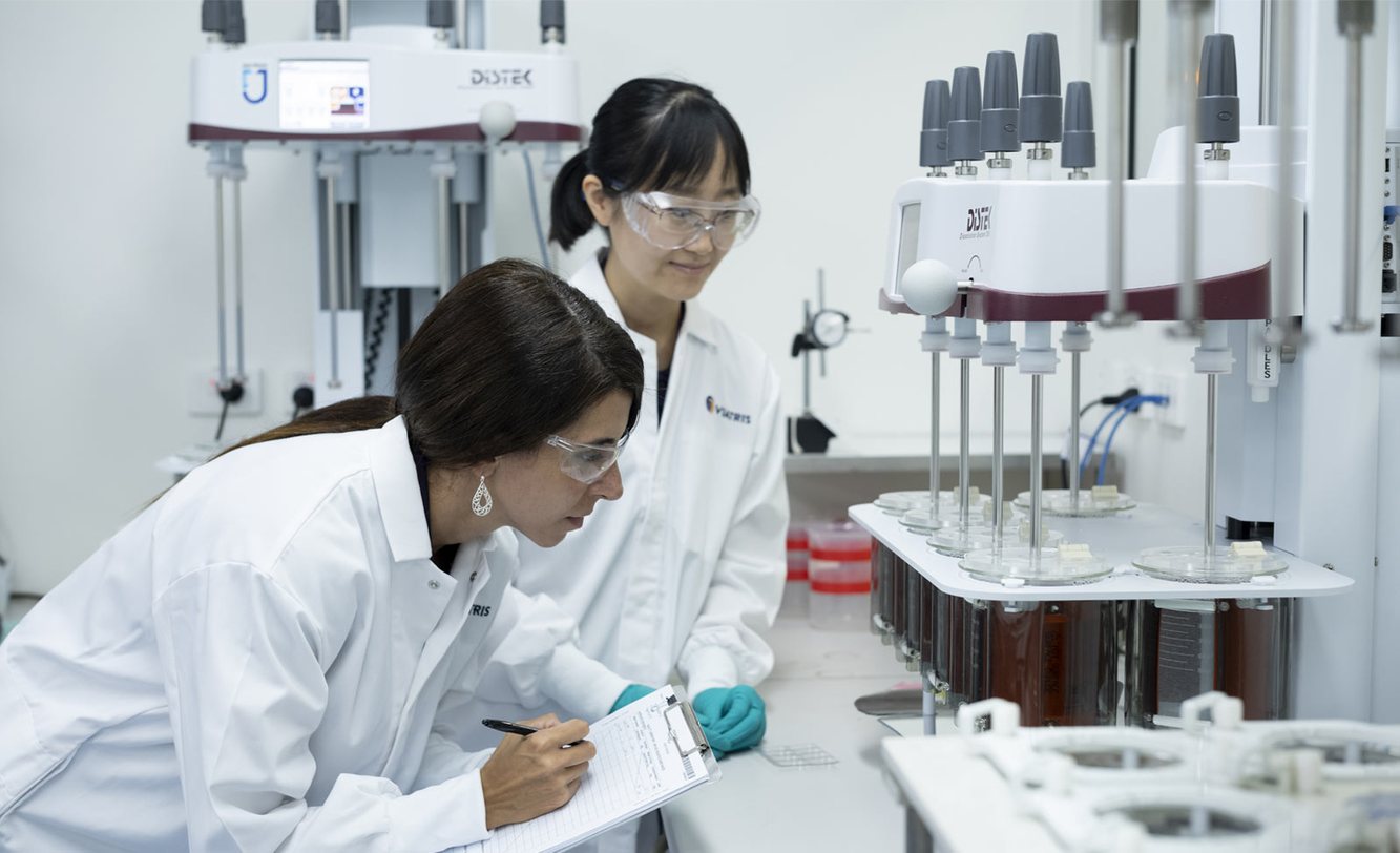 Two Viatris scientists in Viatris lab coats reviewing notes beside lab instruments